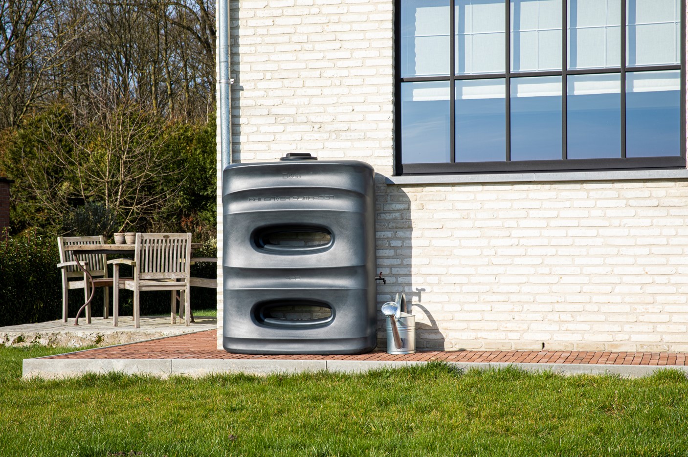 Een kunststof regenwaterput staat in de tuin met een gieter ernaast.